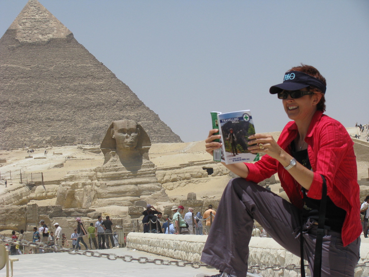 An image of a woman reading the Travelling Well Book with a pyramid behind her
